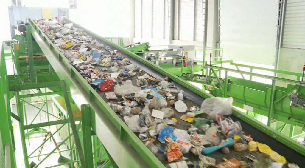 Déchets solides circulant sur un tapis roulant vert dans une usine de tri ou de recyclage visible en intérieur lumineux