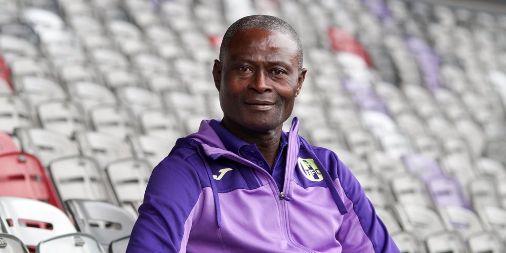Un homme portant une veste de sport violette est assis dans des gradins vides d'un stade