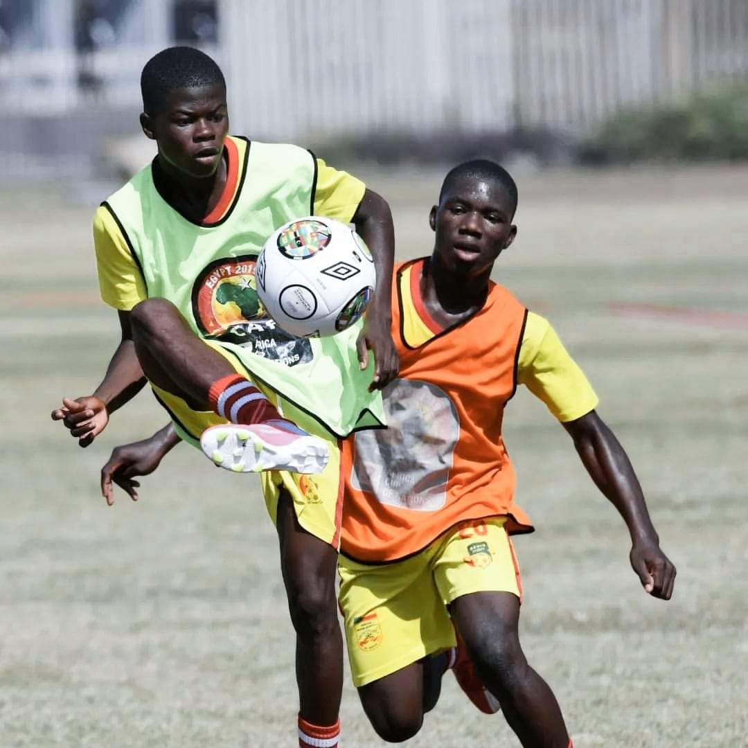 Deux jeunes joueurs en maillots jaunes et chasubles orange et vert se disputent un ballon en plein match sur un terrain de football