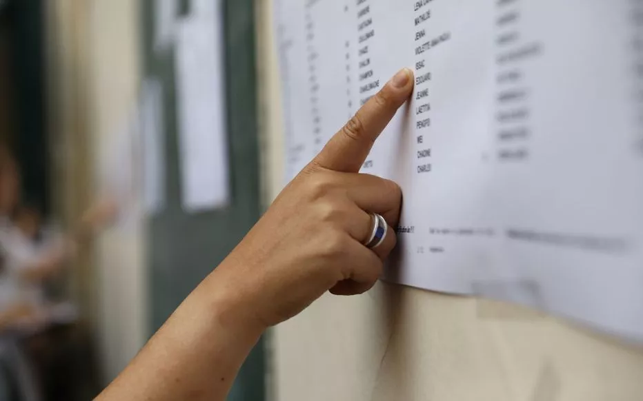 Doigt pointant une ligne sur une feuille blanche affichée sur un mur extérieur flouté en arrière-plan