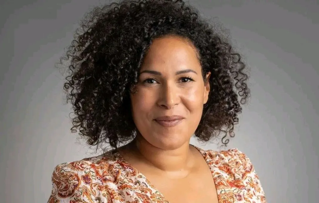Femme souriante aux cheveux bouclés portant une robe à motifs floraux sur fond gris uniforme