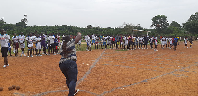 Un groupe de personnes alignées sur un terrain de sport en terre battue avec un joueur lançant un objet vers un point donné