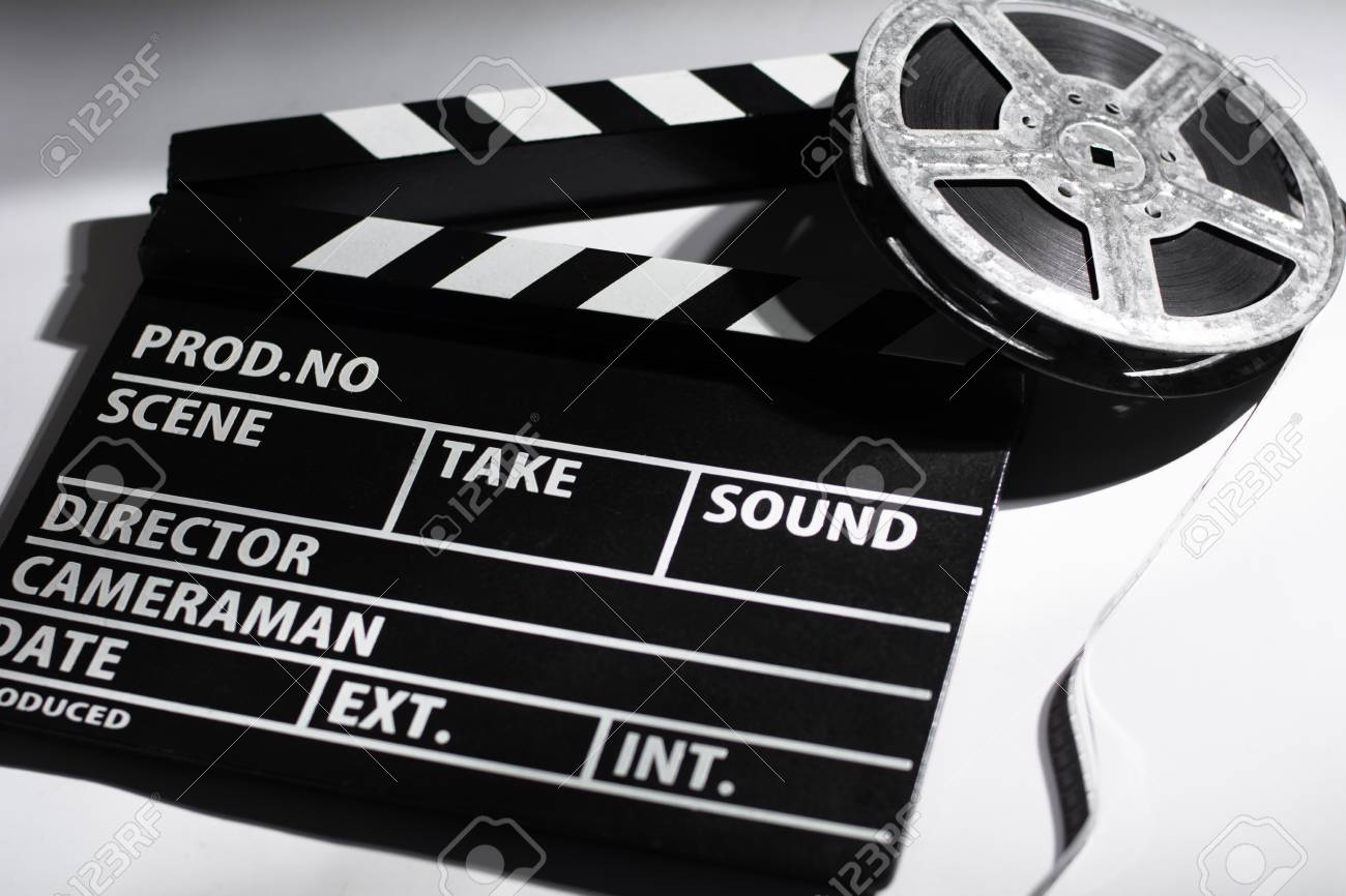 Clap de cinéma noir et blanc et une bobine de film argentique posés sur une surface blanche