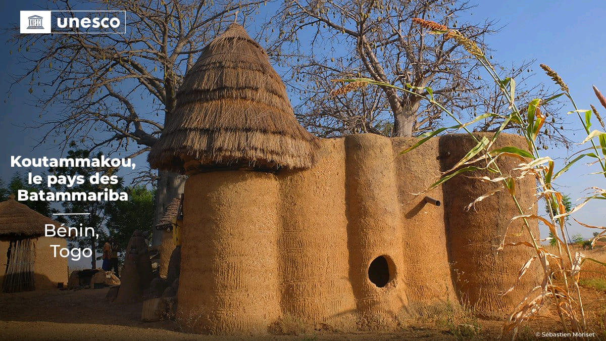 Habitat traditionnel en terre avec toiture en chaume sous un ciel bleu et arbres autour en pleine journée