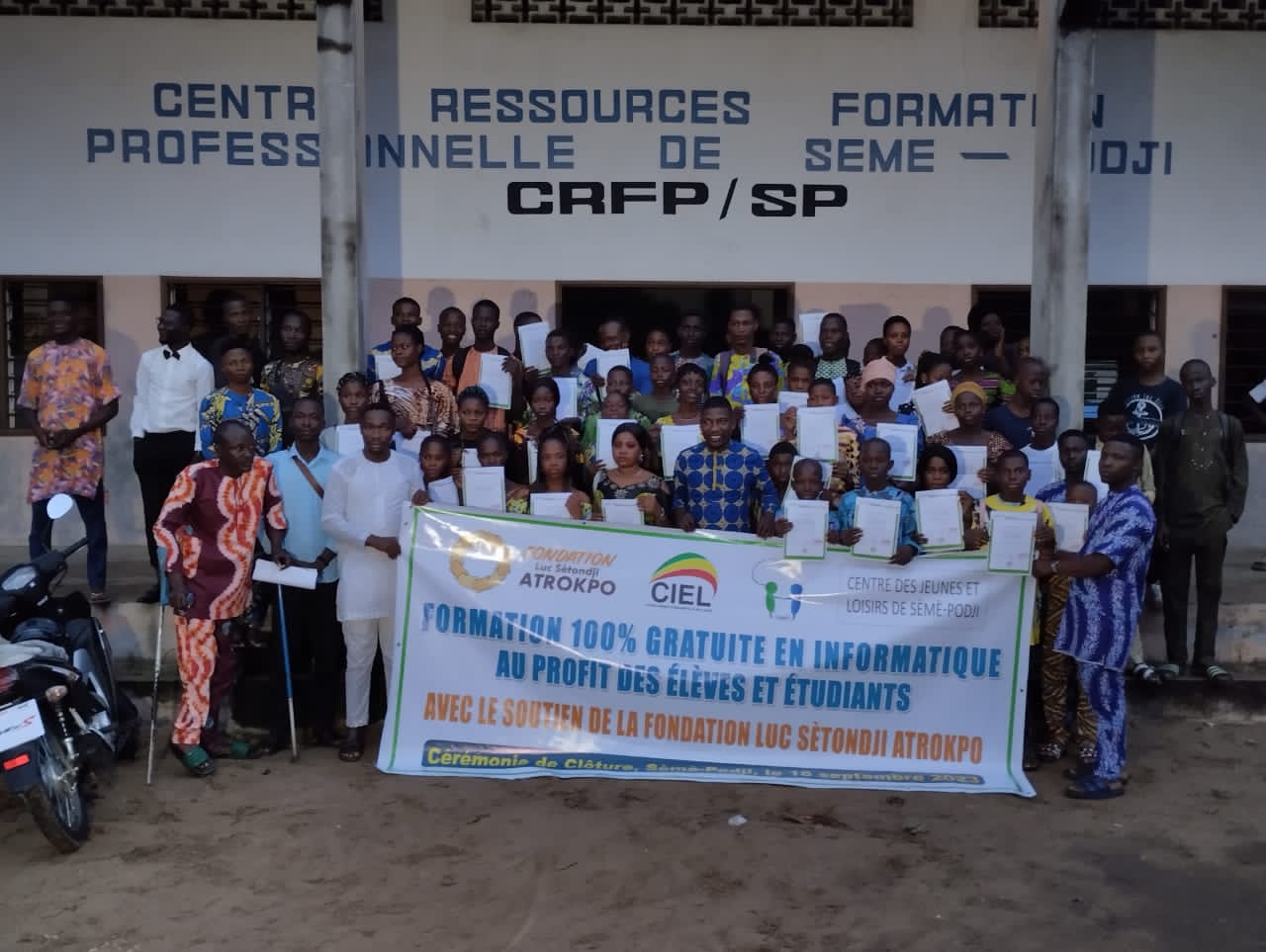 Groupe de jeunes et adultes posant devant un bâtiment avec une grande banderole de formation gratuite en informatique