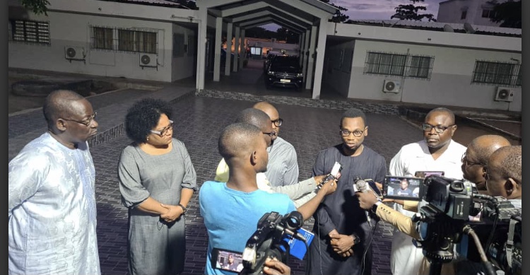 Un groupe de personnes discute devant des microphones et des caméras dans une cour extérieure au crépuscule