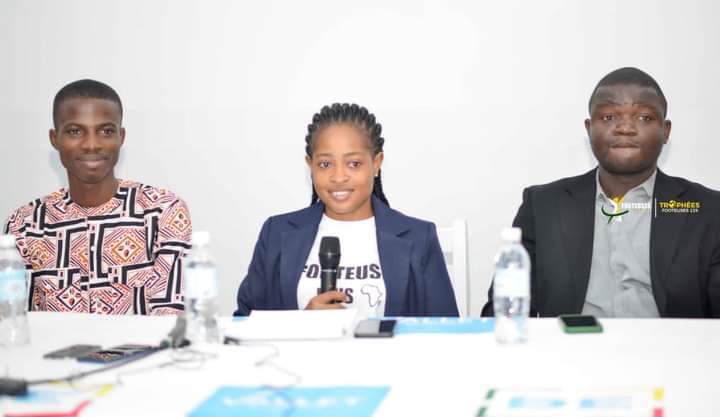 Trois personnes assises derrière une table avec micro et bouteilles d'eau lors d'une conférence ou réunion