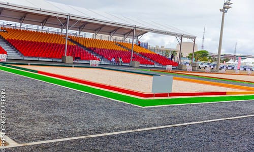 Terrain de pétanque délimité en sable avec tribunes vides aux sièges rouge et orange en arrière-plan