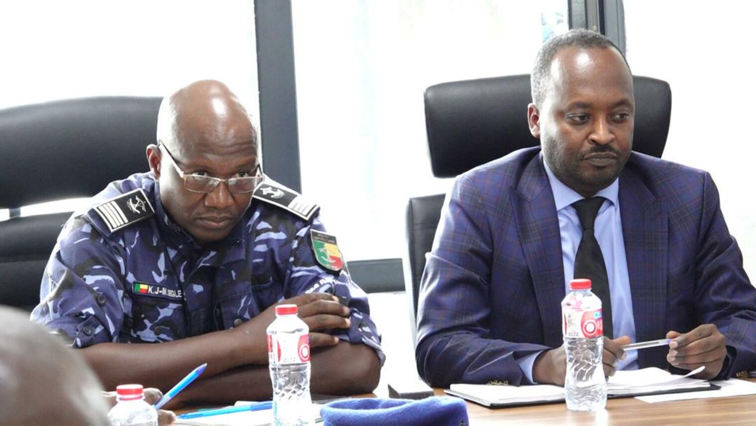 Deux hommes assis à une table lors d'une réunion avec des bouteilles d'eau devant eux et des carnets ouverts
