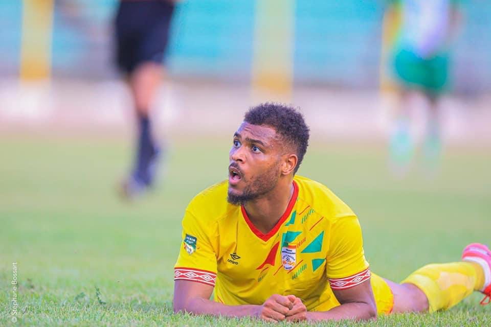 Un joueur en maillot jaune est allongé sur le terrain de football en regardant vers le haut avec une expression surprise