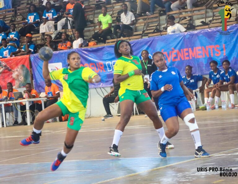 Trois joueuses de handball en action sur le terrain lors d'un match devant des spectateurs assis dans les gradins