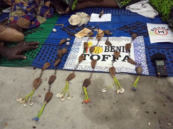 Objets artisanaux traditionnels posés sur une toile colorée près de mains et pieds visibles au sol