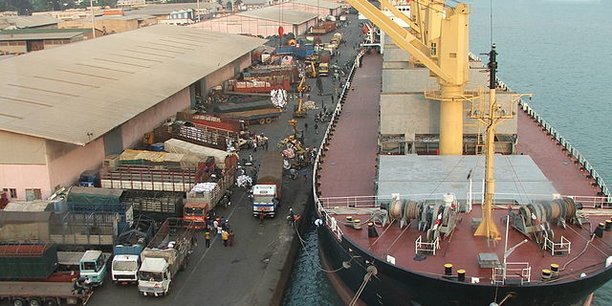 Vue aérienne d’un port avec un grand cargo amarré à quai et plusieurs camions stationnés le long du déchargement