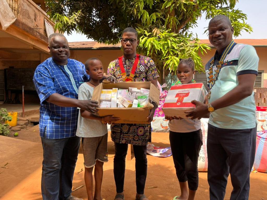 Quatre personnes et deux enfants debout dehors tenant des boîtes de fournitures alimentaires et de soins sous un arbre