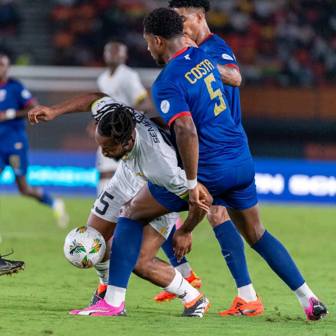 Deux joueurs en maillots bleus disputent le ballon avec un joueur en maillot blanc sur un terrain de football en pleine action