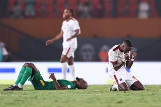 Deux joueurs de football au sol et à genoux exprimant des émotions fortes pendant un match sur un terrain vert