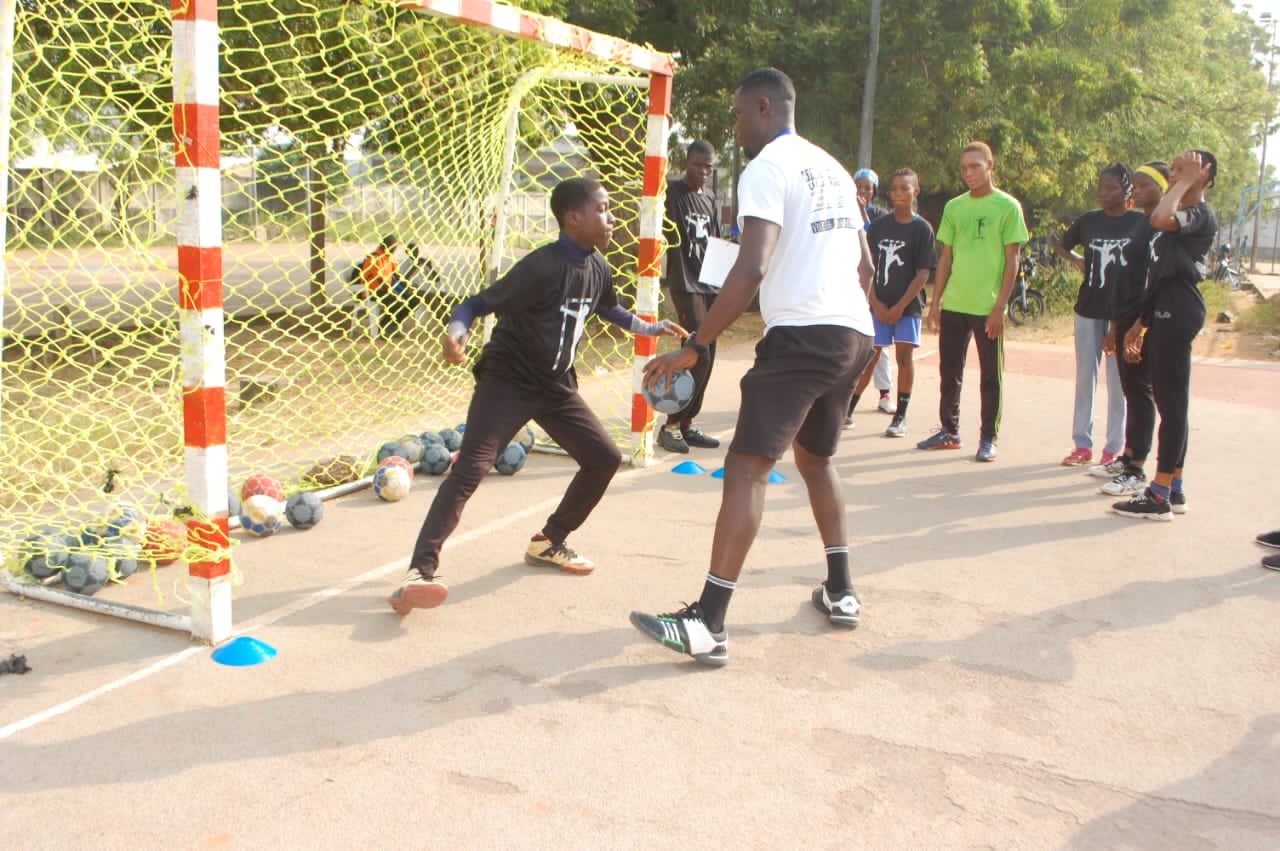 Un jeune joueur de handball s'entraîne comme gardien de but devant un groupe observateur lors d'une séance en plein air