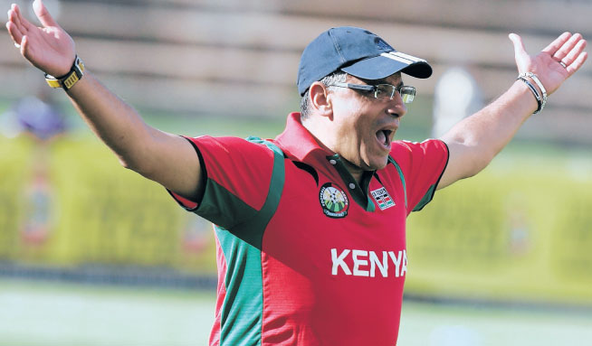 Homme en polo rouge avec inscription Kenya et casquette bleue fait un geste d’exclamation avec les bras écartés