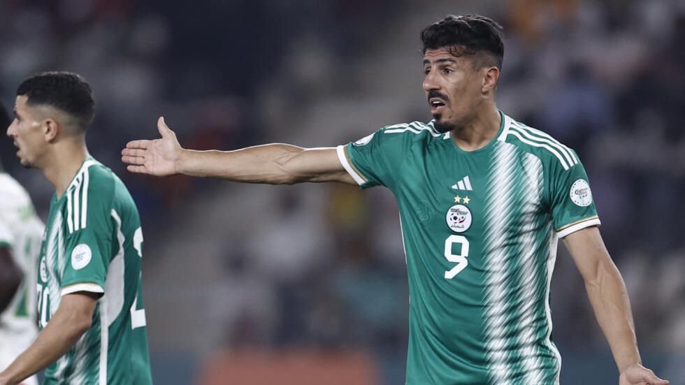 Deux joueurs en maillot vert discutent sur un terrain de football lors d'un match nocturne