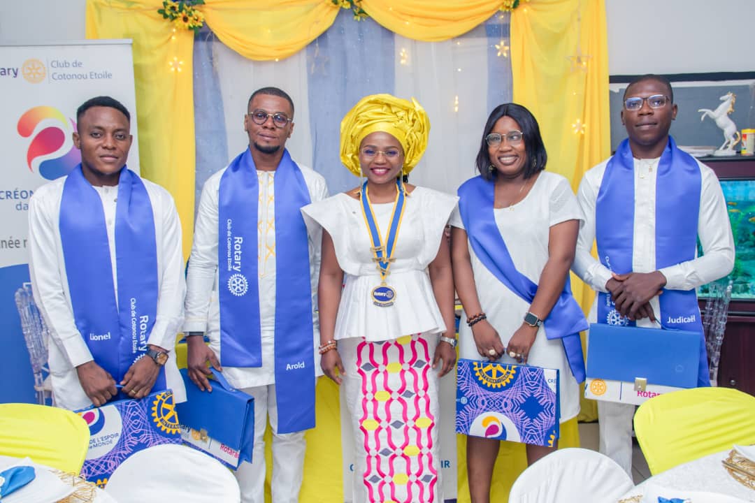 Cinq personnes habillées en tenue traditionnelle et écharpes bleues posent devant un décor jaune et blanc festif