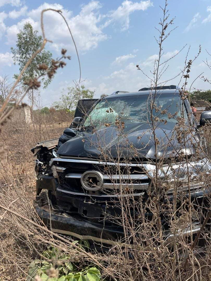 Véhicule noir accidenté avec pare-brise fissuré et calandre endommagée dans un champ sec avec des herbes hautes