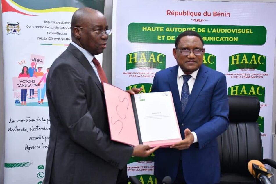 Deux hommes en costume échangent un document devant des panneaux officiels sur la communication et l'audiovisuel