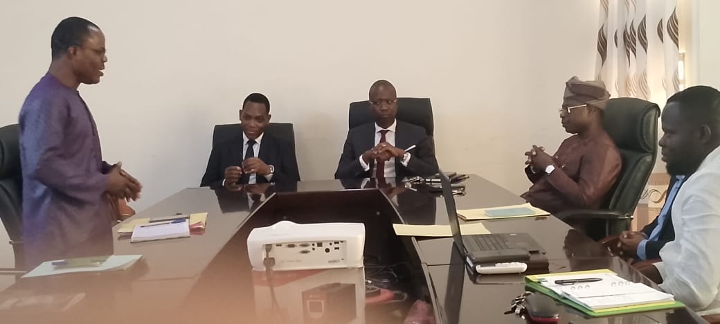 Cinq hommes en réunion assis autour d’une grande table avec documents et un ordinateur portable posé dessus