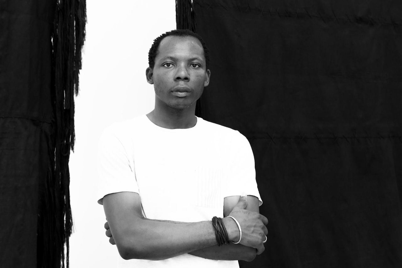 Homme noir en t-shirt blanc bras croisés devant un fond sombre lisse et uniforme