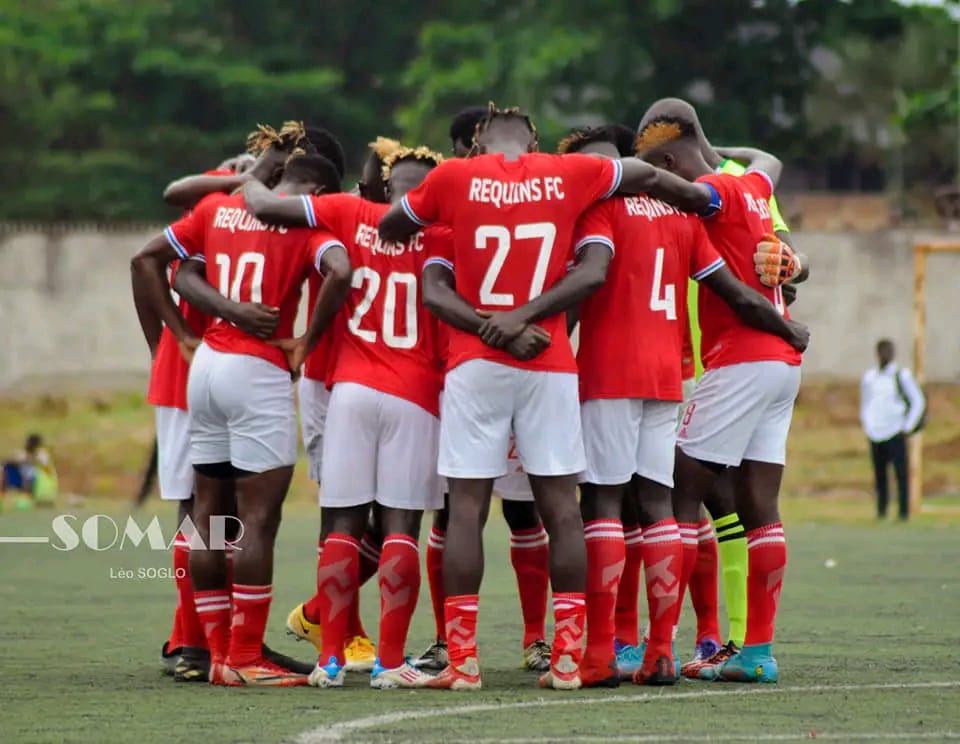 Joueurs en maillot rouge formant un cercle de cohésion sur un terrain de football gazonné