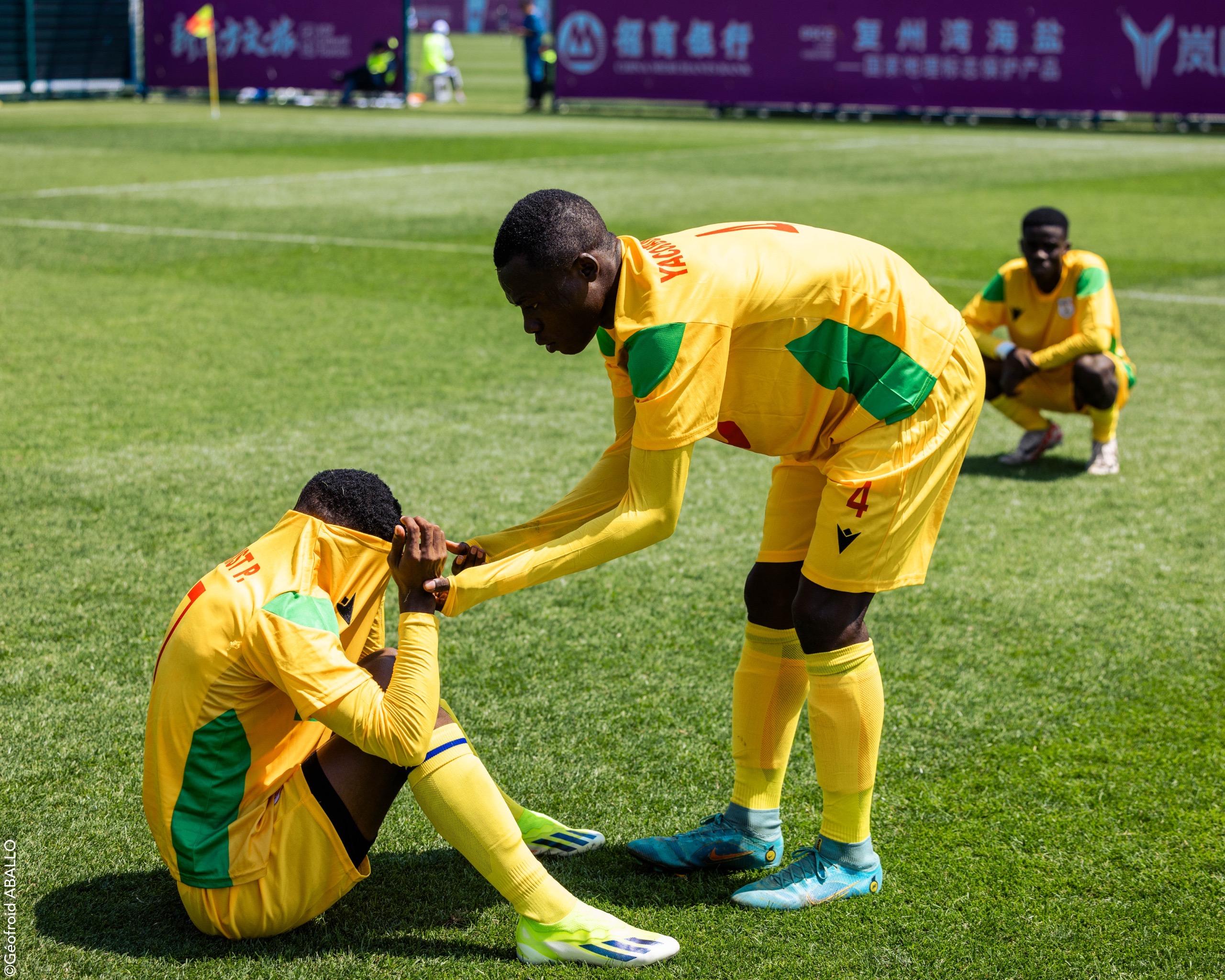 Trois joueurs de football en tenue jaune et verte montrent de la déception sur le bord du terrain de jeu en herbe verte