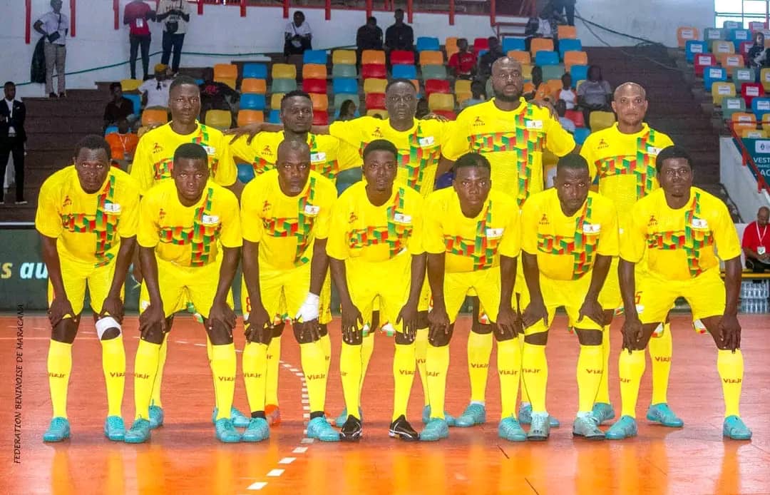 Onze joueurs en tenue jaune posent ensemble sur un terrain de futsal devant des gradins multicolores et un public clairsemé