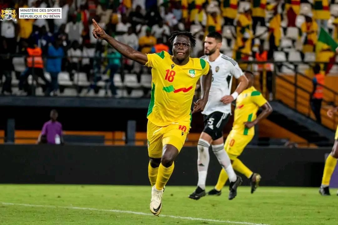Un joueur en maillot jaune numéro 18 célèbre en courant avec le bras droit levé sur un terrain de football pendant un match.