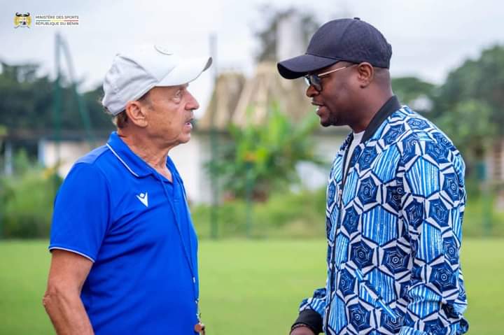 Deux hommes discutent dehors, l’un porte une casquette blanche et un polo bleu, l’autre une casquette noire et un vêtement à motifs bleus