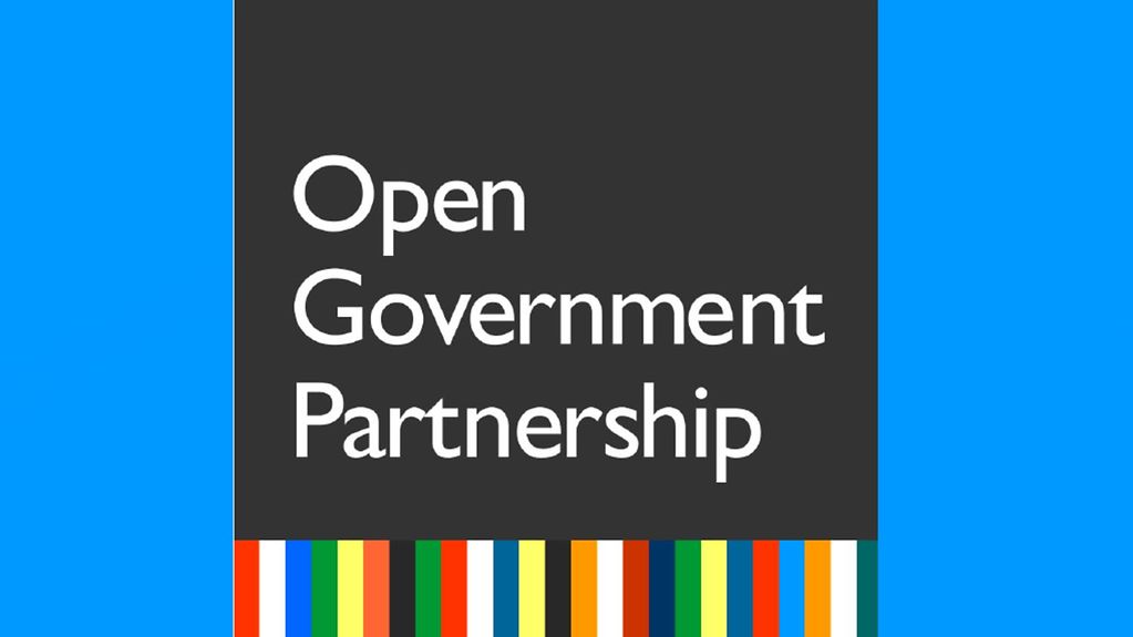 Logo blanc Open Government Partnership sur fond noir avec des bandes colorées en bas et fond bleu sur les côtés