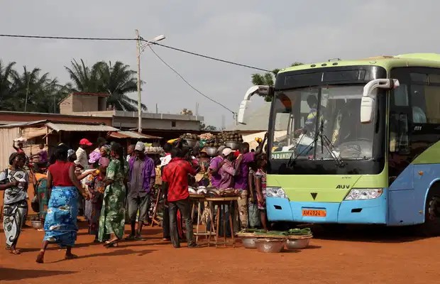 Un bus stationné près d’un marché en plein air avec plusieurs personnes vêtues de tenues colorées autour