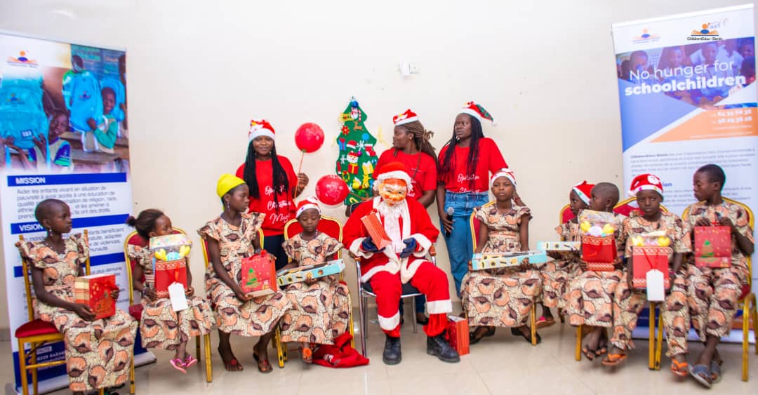 Un groupe d’enfants en tenue assortie et plusieurs adultes avec chapeaux de Noël posent autour d’un Père Noël et d’un sapin décoré