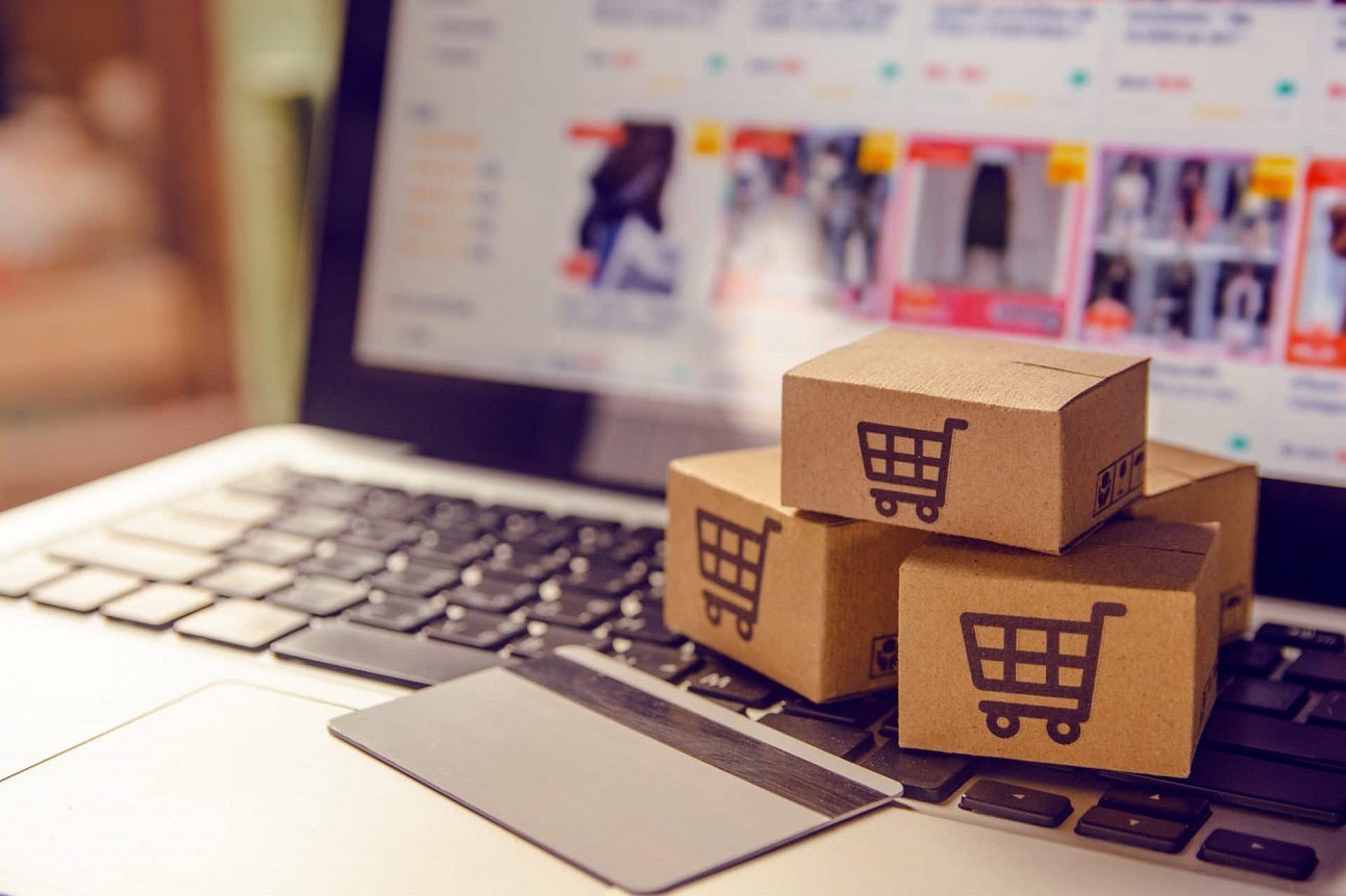 Trois petites boîtes en carton avec un symbole de caddie empilées sur un clavier d'ordinateur portable avec une carte bancaire posée dessus
