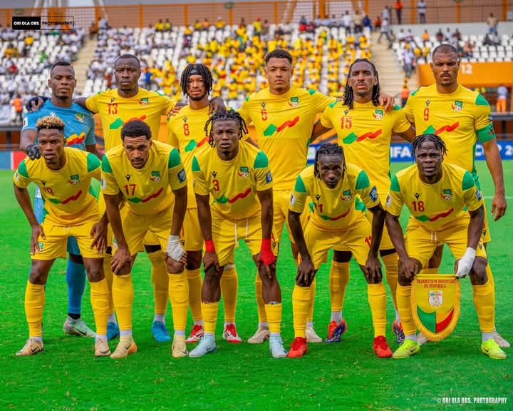 Onze joueurs de football en tenue jaune posant sur le terrain avant un match avec tribunes remplies en arrière-plan