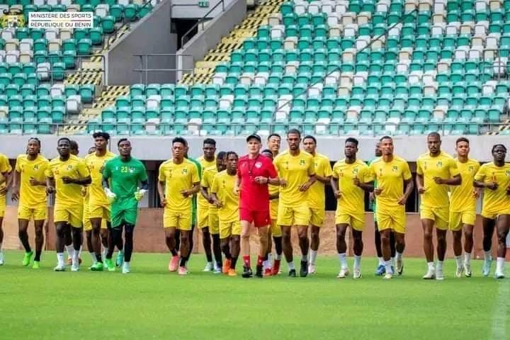 Groupe de joueurs de football en tenue de sport jaune courant sur un terrain dans un stade aux gradins verts et blancs