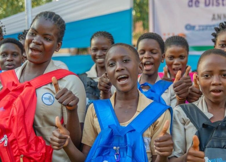 Un groupe de jeunes élèves souriants portant des sacs à dos colorés montrent des pouces levés en extérieur