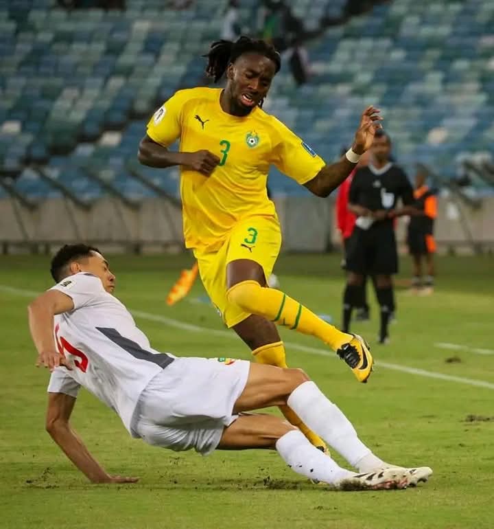 Un joueur en jaune dribble face à un adversaire en blanc qui effectue un tacle glissé sur le terrain de football