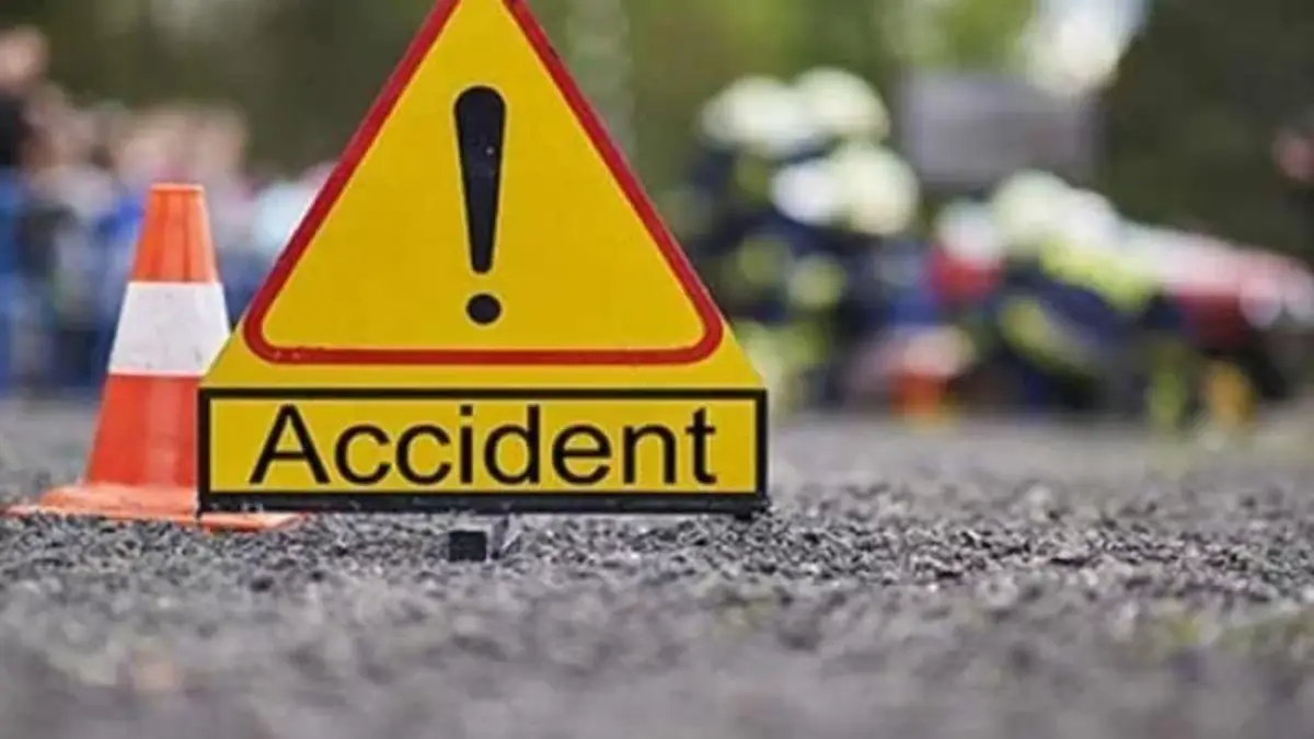 Panneau triangulaire jaune "Accident" posé sur une route avec un cône orange et une foule floue en arrière-plan