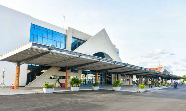Façade d’un terminal d’aéroport moderne avec des plantes en pots alignées devant le bâtiment sous un auvent gris