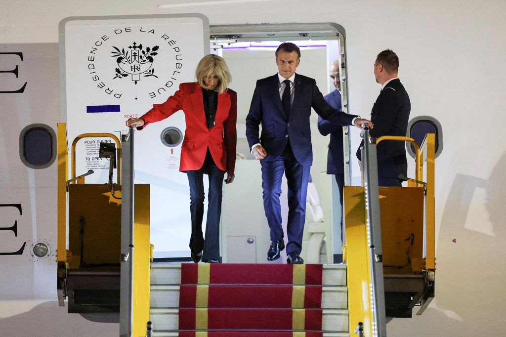 Un homme en costume bleu descend les marches d’un avion officiel précédé d’une femme en veste rouge et pantalon noir