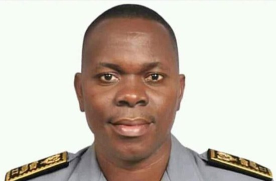 Homme en uniforme gris avec une épaulette noire et or souriant face à l’objectif sur fond clair