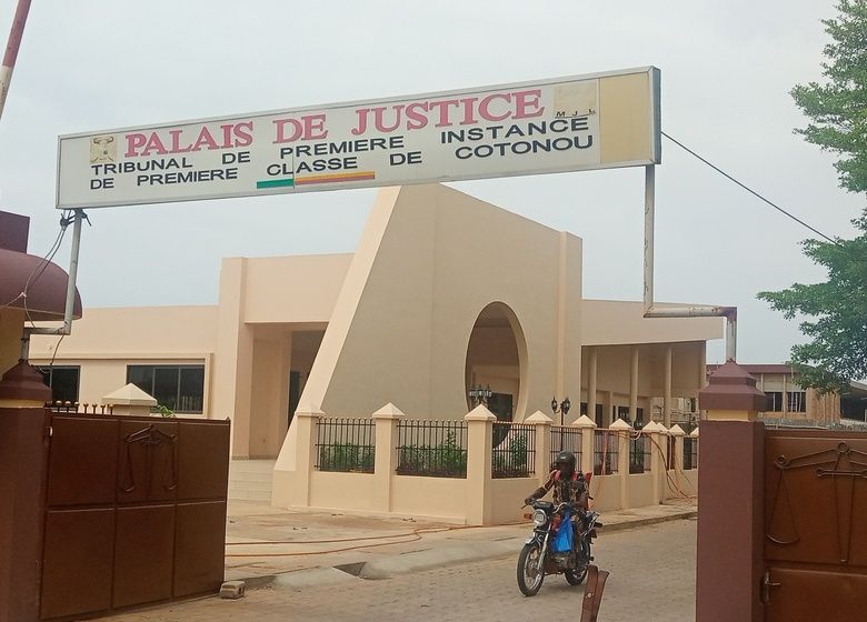 Façade d un bâtiment avec un panneau intitulé Palais de Justice Tribunal de Première Instance Classe de Cotonou et un homme à moto devant