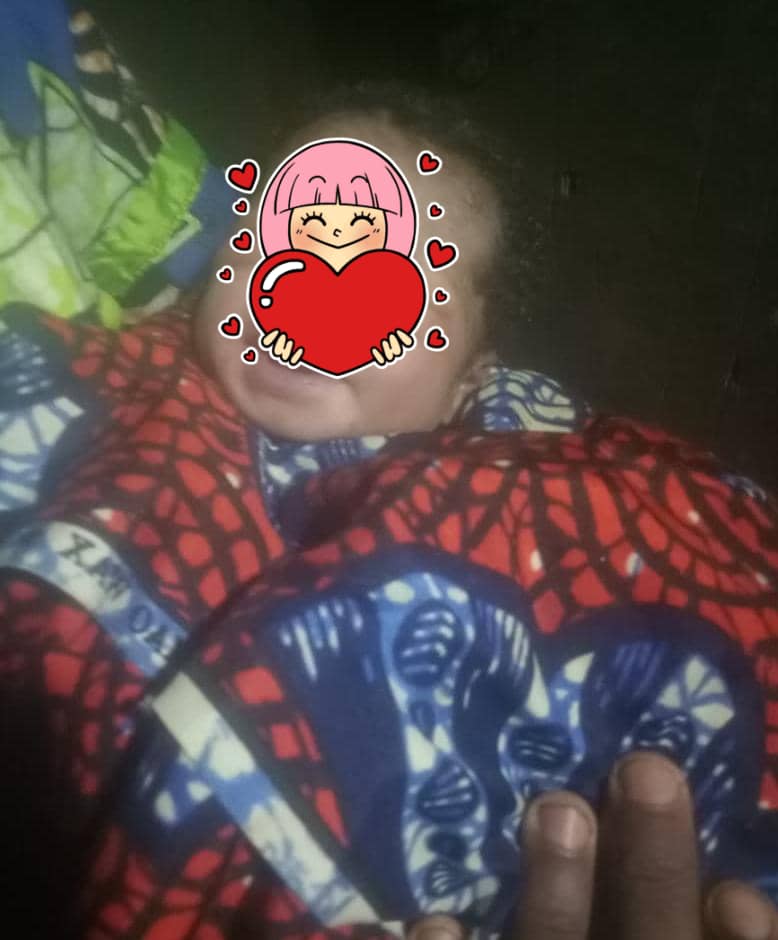 Nourrisson emmailloté dans un tissu coloré soutenu par une main posée sur sa poitrine avec visage recouvert d’un dessin emoji