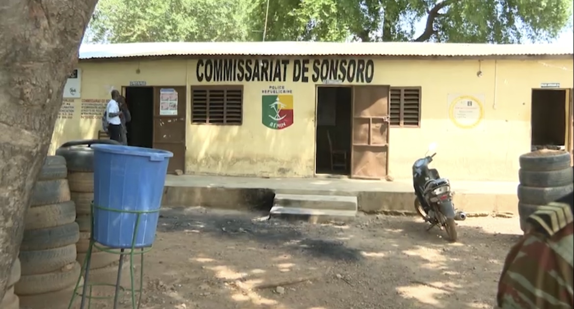 Façade d un bâtiment de commissariat avec un homme devant une porte ouverte et une moto garée à proximité