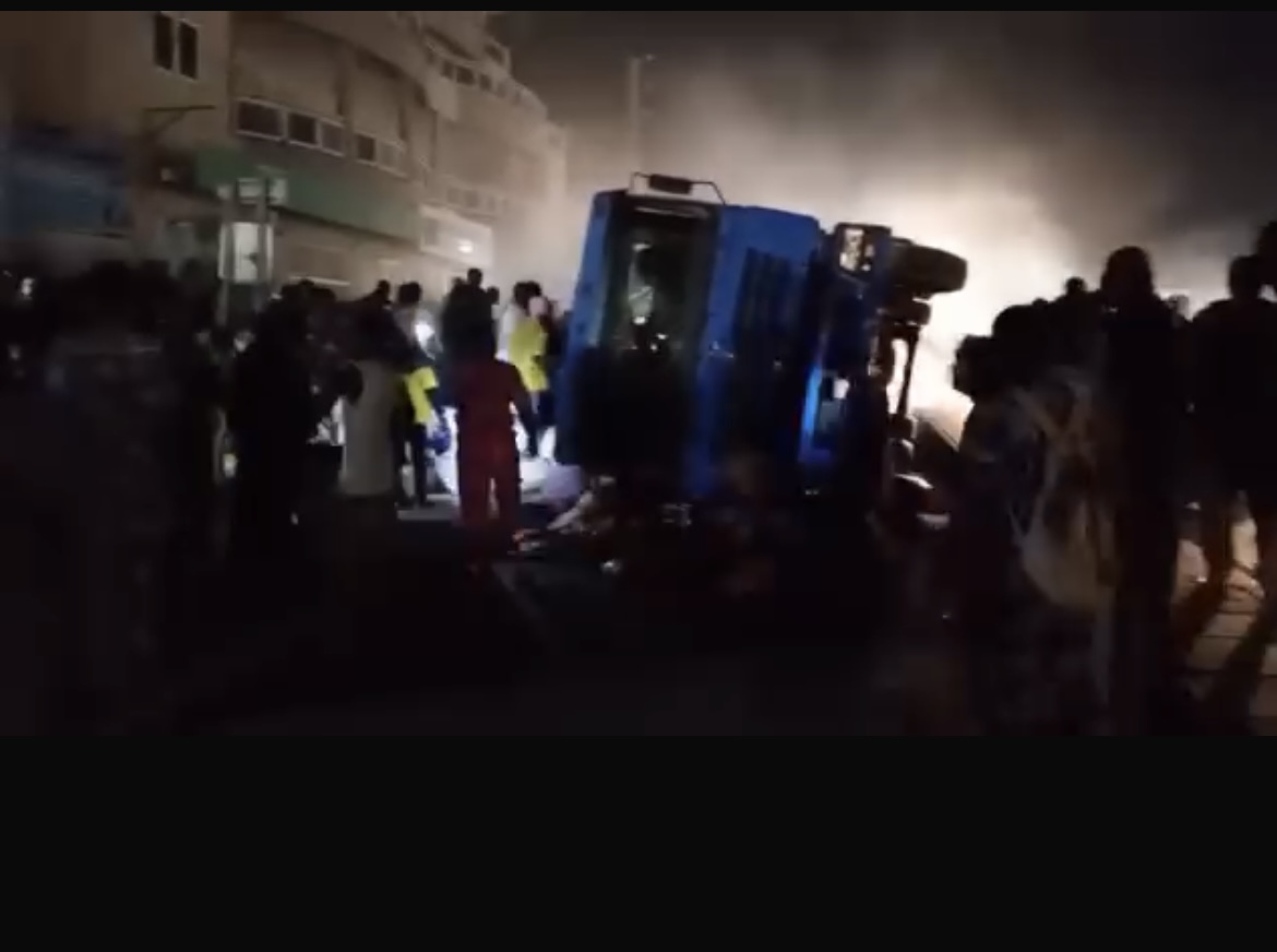 Camion renversé sur le côté entouré de plusieurs personnes dans une rue obscure éclairée par des phares