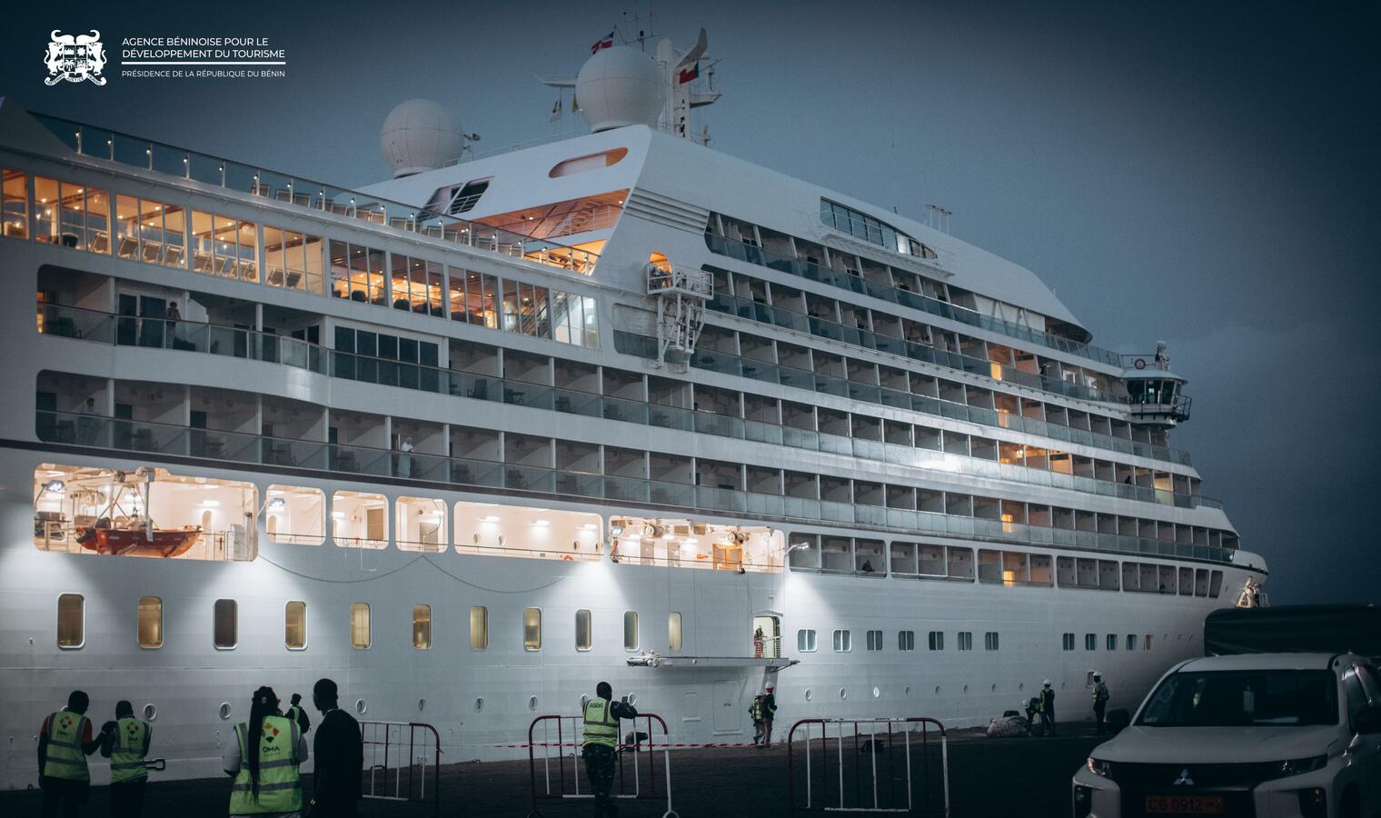 Navire de croisière blanc amarré la nuit avec plusieurs personnes en gilet réfléchissant sur le quai près du bateau